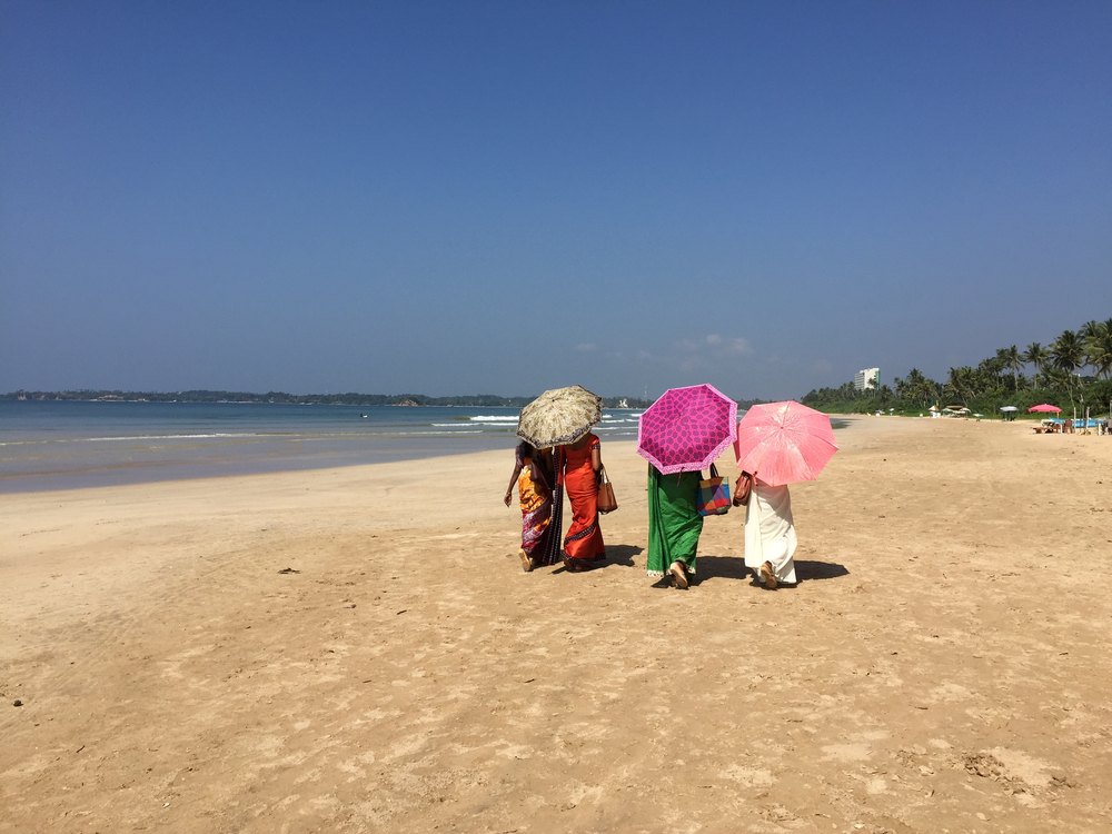 Women with traditional clothes walking on the beach at Weligama bay